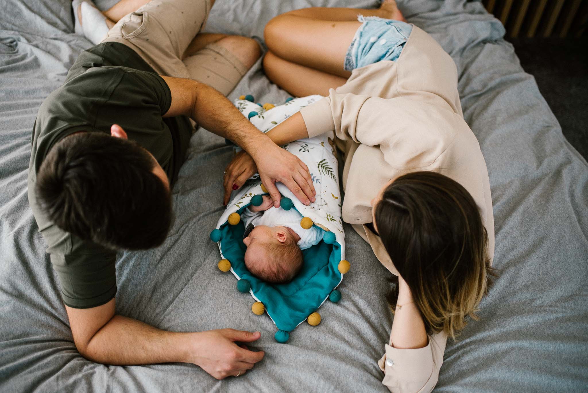 Rodzice leżą z noworodkiem na łóżku - sesja noworodkowa lifestyle w Poznaniu