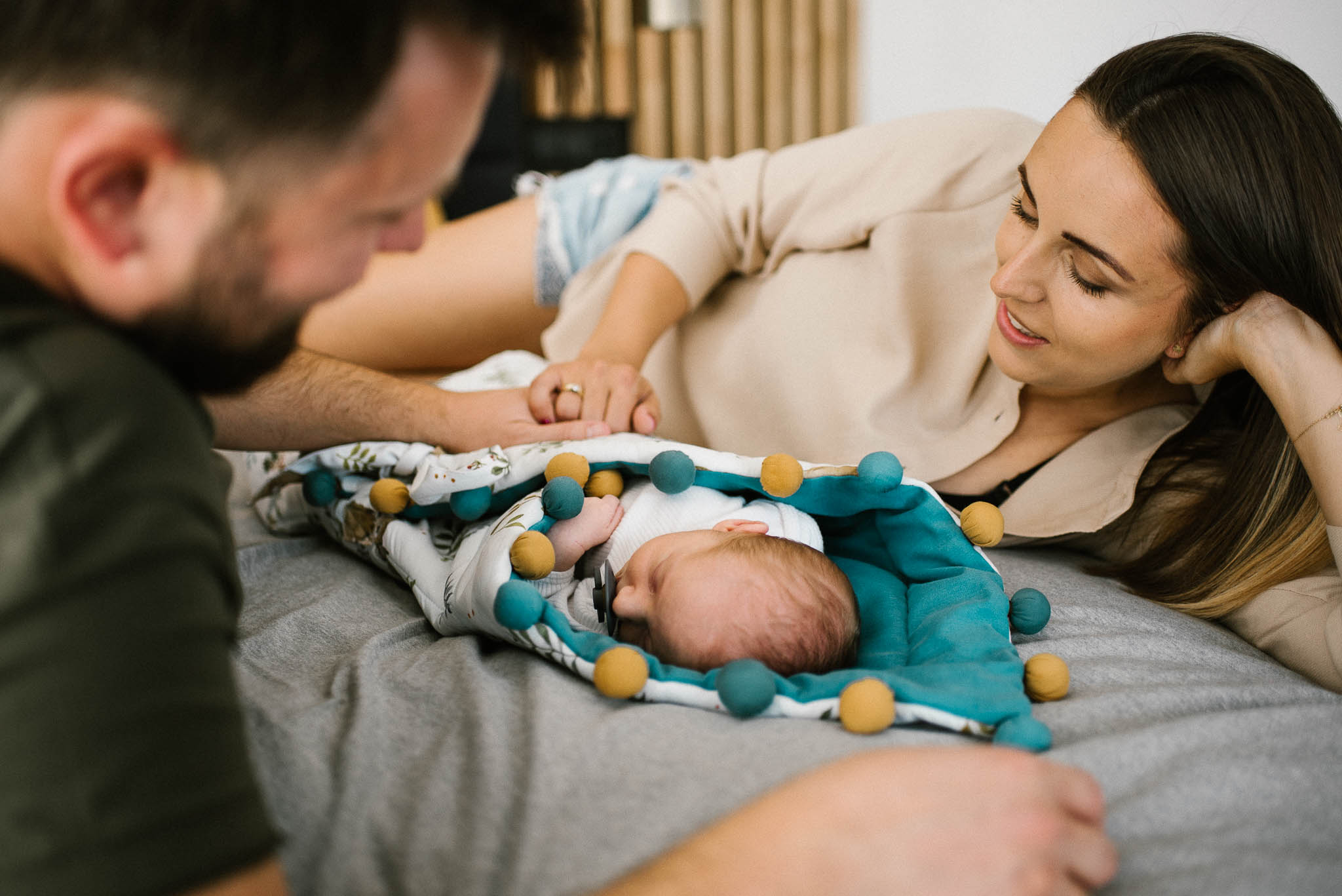 Rodzice leżą na łóżku i patrzą na noworodka - sesja noworodkowa lifestyle w Poznaniu