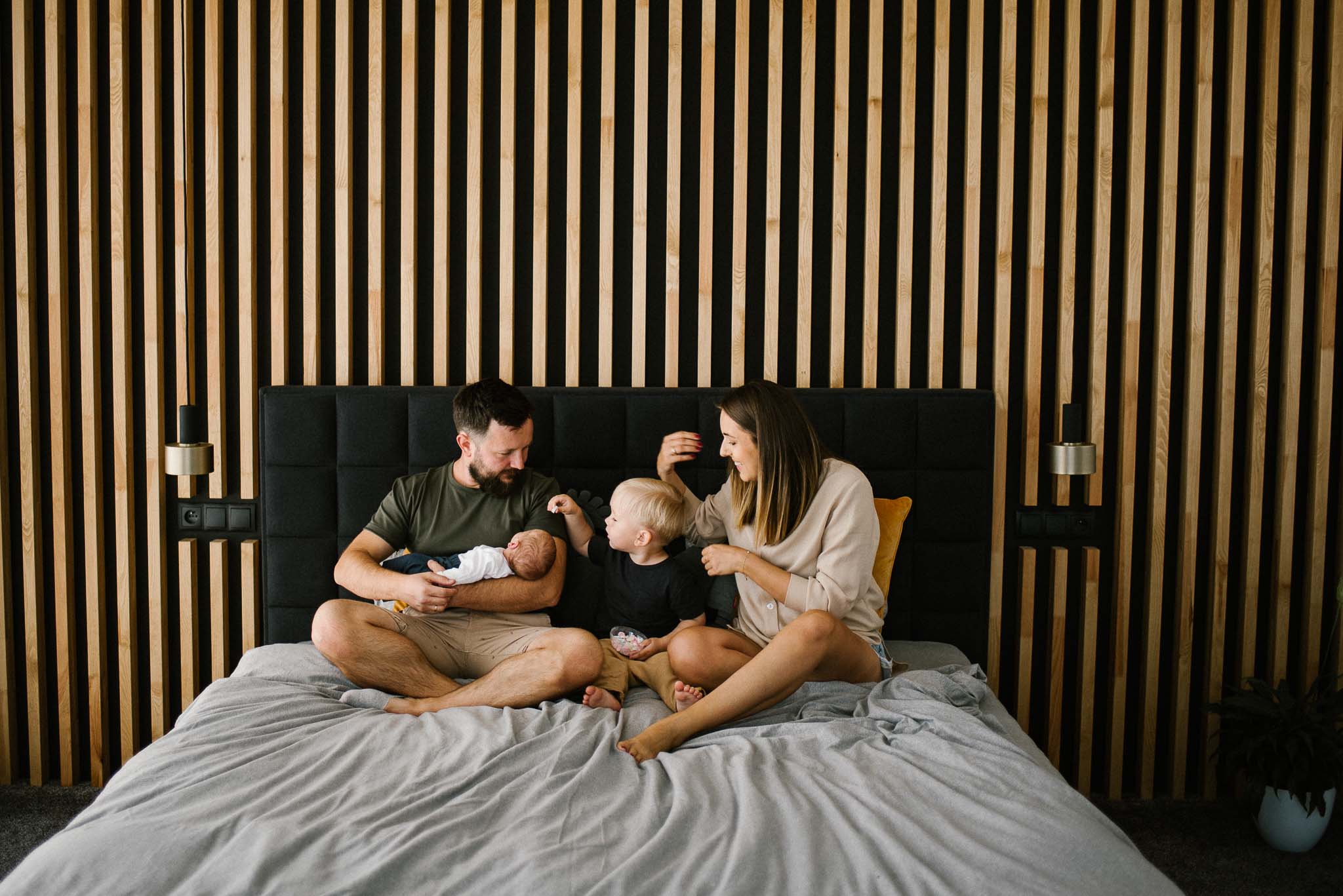 Rodzina siedzi na łóżku z niemowlakiem - sesja noworodkowa lifestyle w Poznaniu