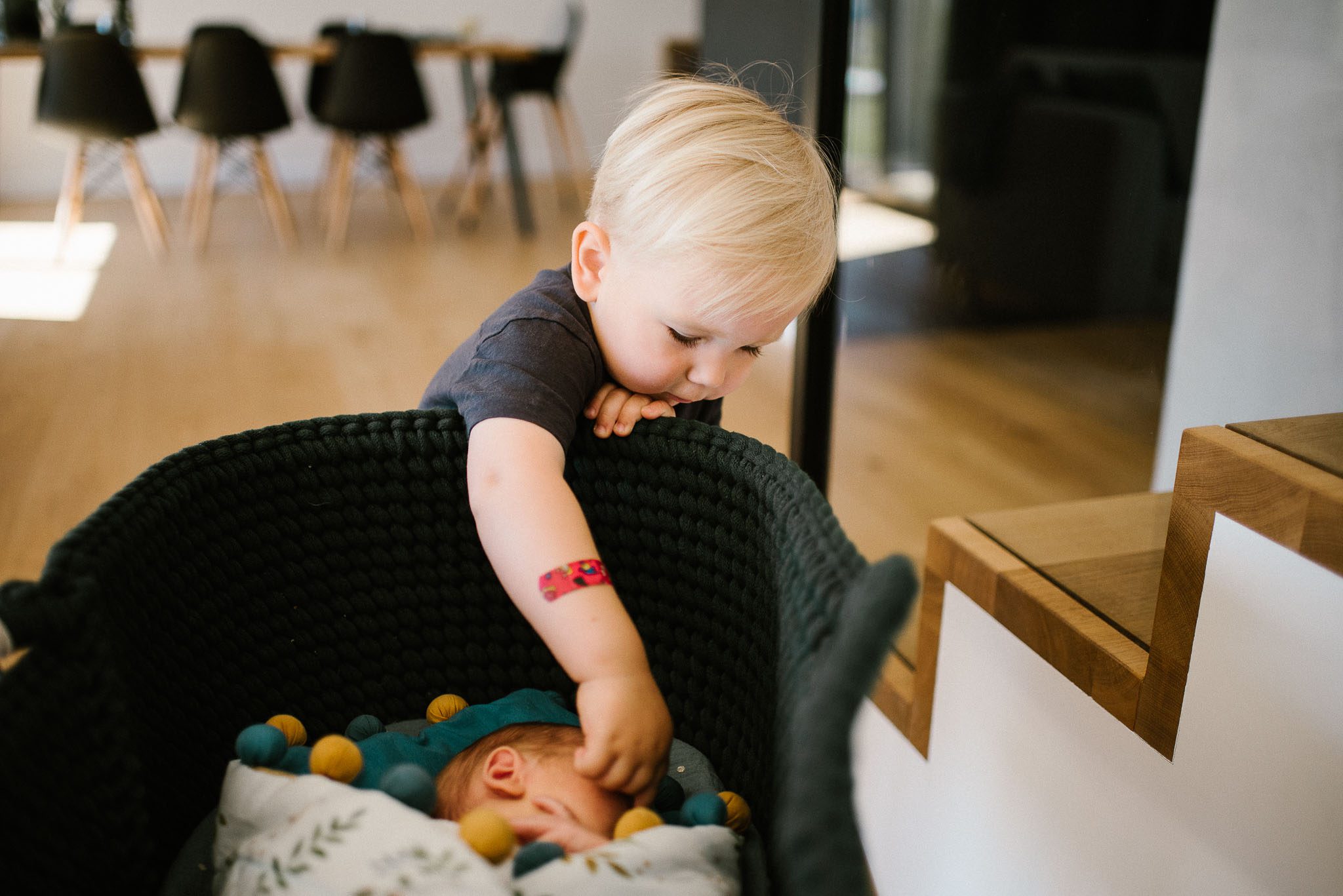 Chłopiec podchodzi do łóżeczka, w którym leży noworodek - sesja noworodkowa lifestyle w Poznaniu