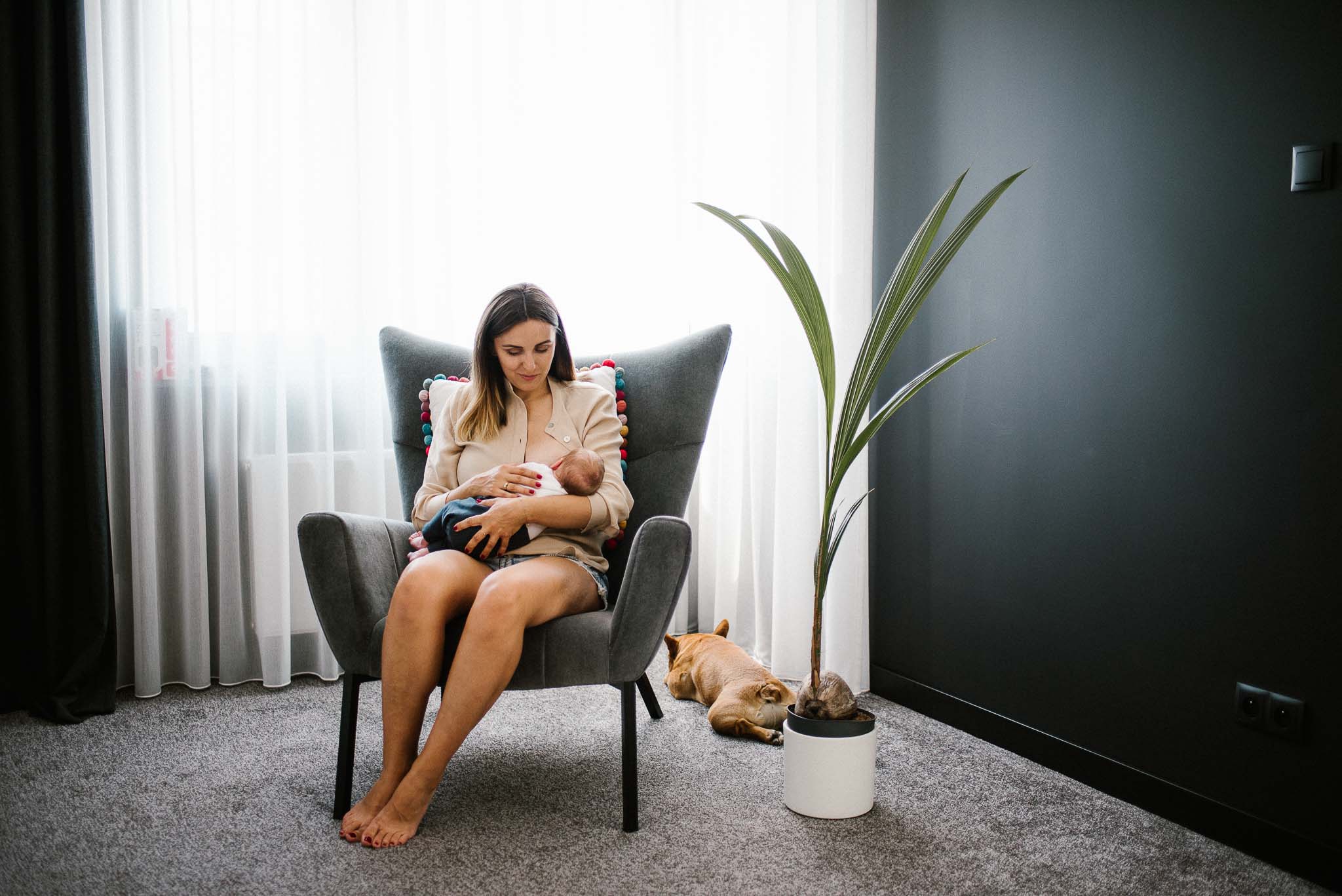 mama karmi noworodka piersią na fotelu - sesja noworodkowa lifestyle w Poznaniu