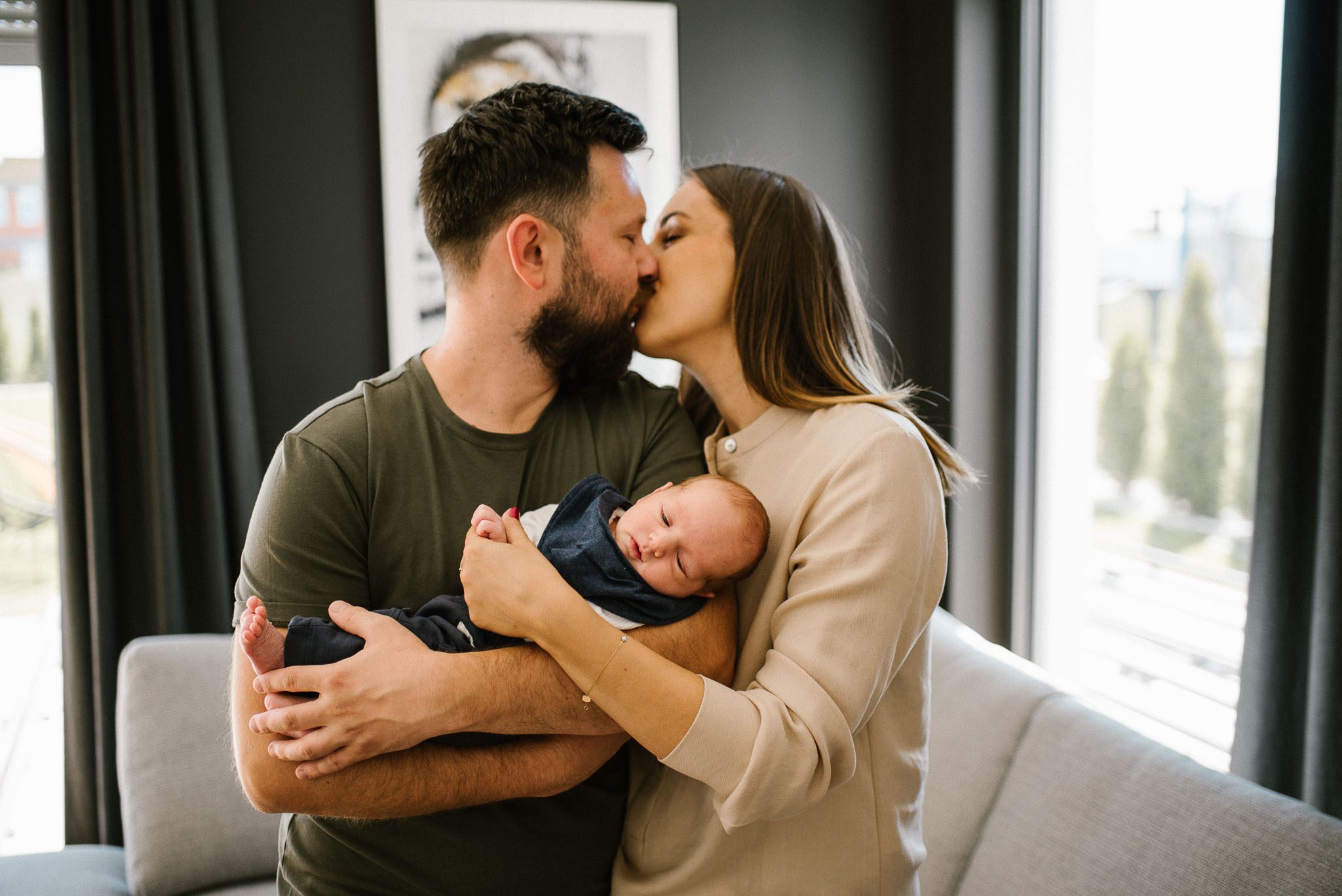 Rodzice trzymają noworodka na rękach i się całują - sesja noworodkowa lifestyle w Poznaniu