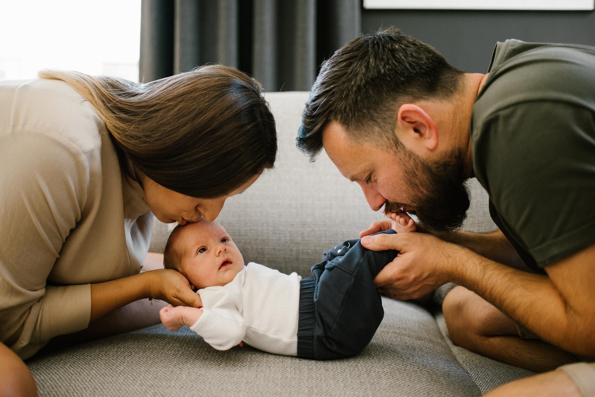 Rodzice patrzą na noworodka na kanapie - sesja noworodkowa lifestyle w Poznaniu