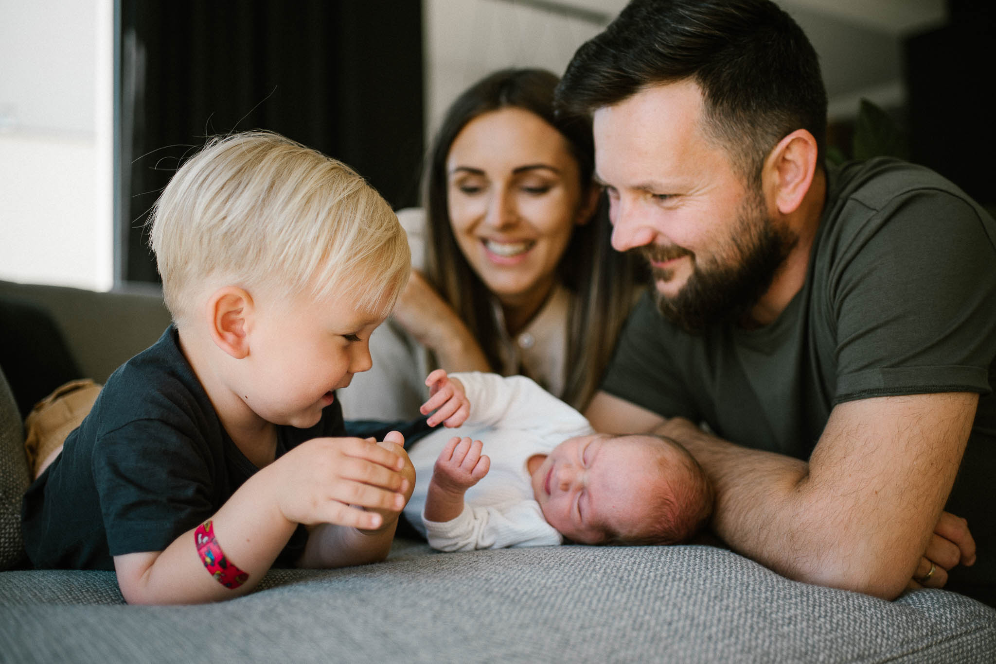 Rodzina z noworodkiem bawią się na kanapie - sesja noworodkowa lifestyle w Poznaniu