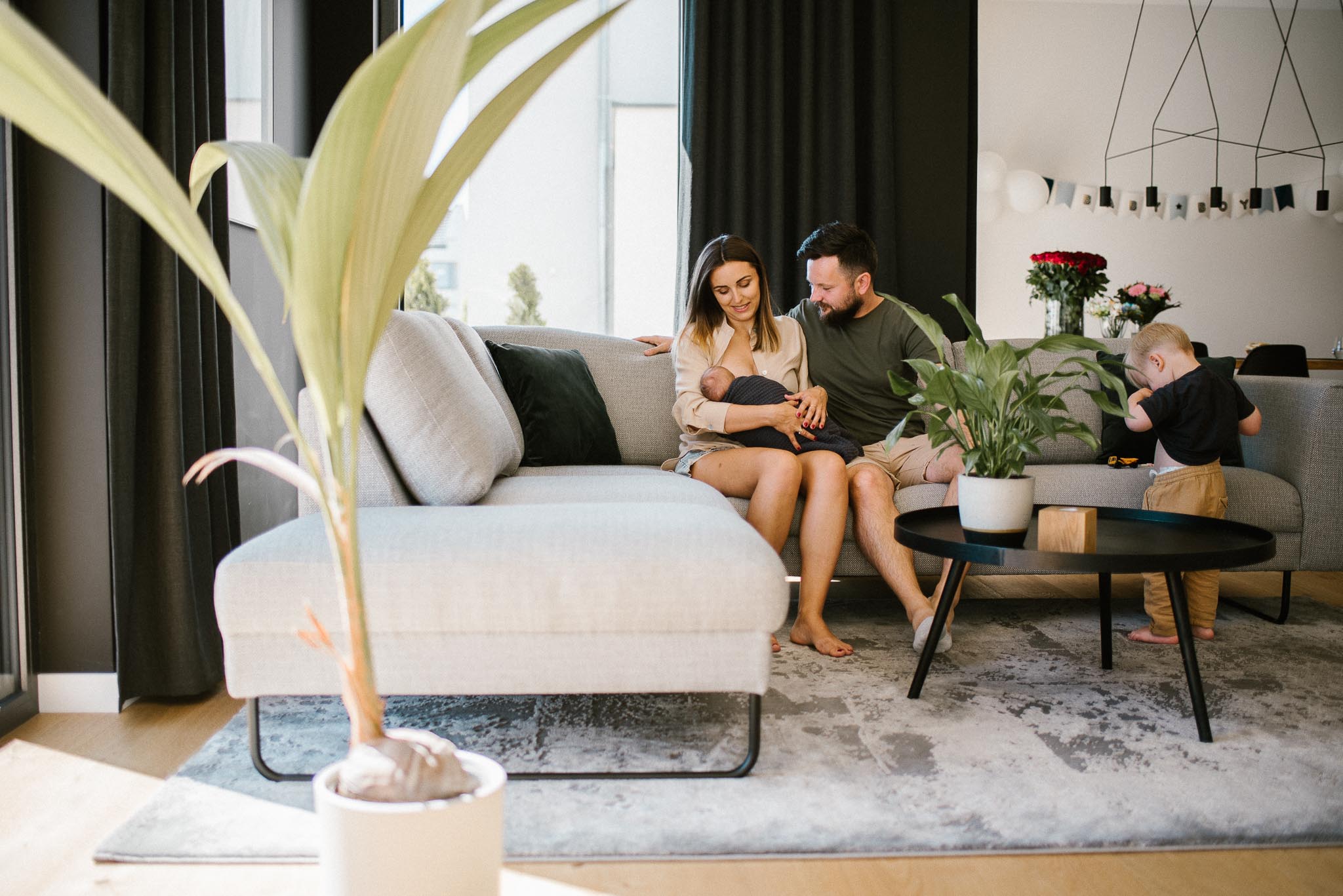 Rodzina z noworodkiem siedzi na kanapie - sesja noworodkowa lifestyle w Poznaniu