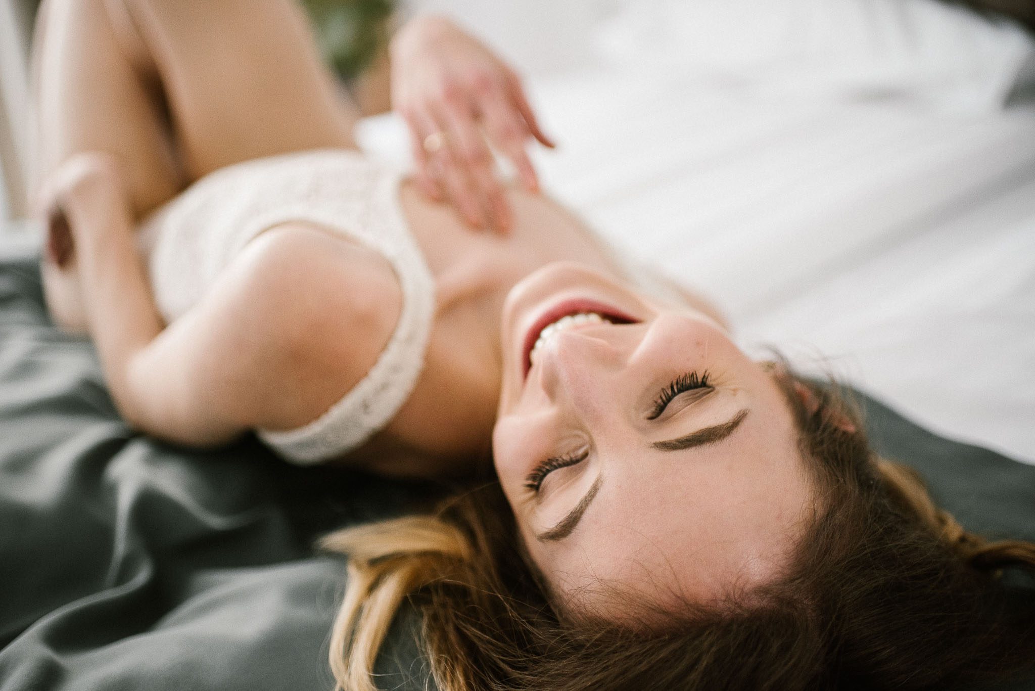 Kobieta na&nbsp;łóżku w&nbsp;bieliźnie gładzi się po&nbsp;dekolcie - sesja kobieca w&nbsp;apartamencie w&nbsp;Poznaniu