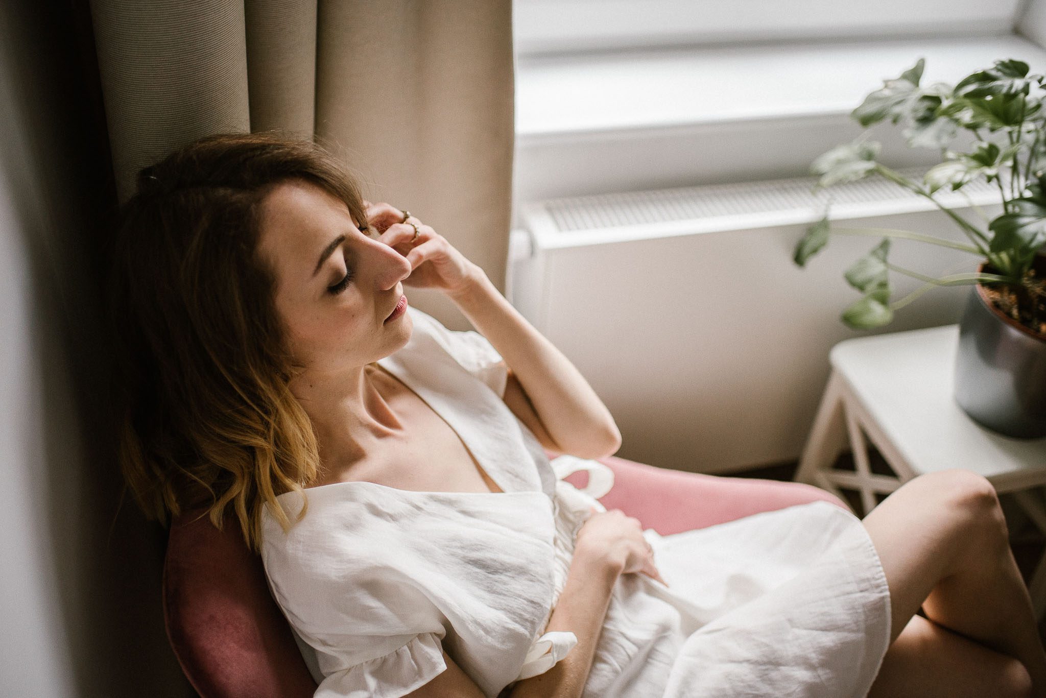 Kobieta siedzi na&nbsp;fotelu w&nbsp;białej sukience podczas kobiecej sesji