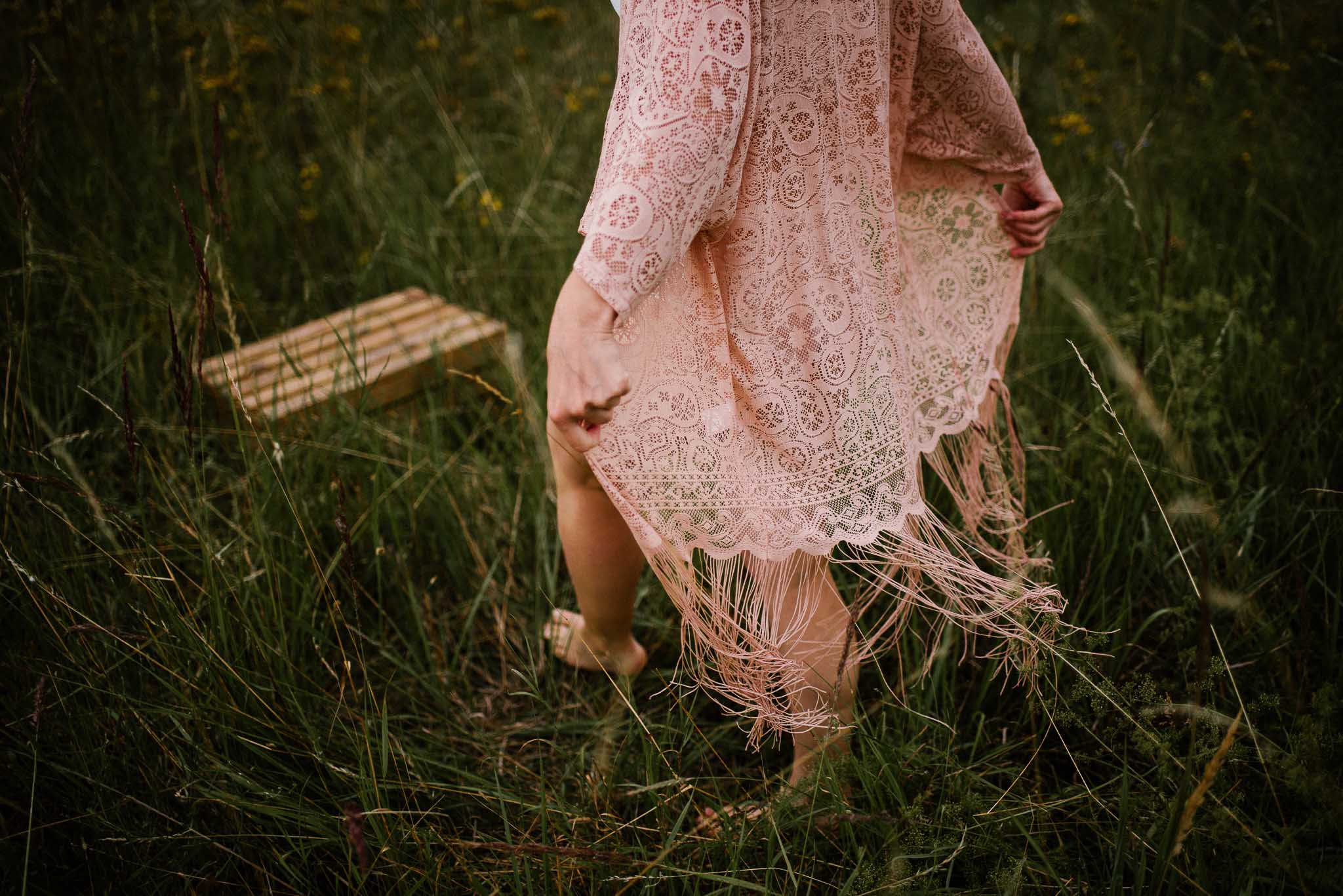 Kobieta idzie przez&nbsp;łąkę w&nbsp;stronę drewnianej skrzyni, zbliżenie na&nbsp;nogi - sesja kobieca sensualna w&nbsp;plenerze Poznań 