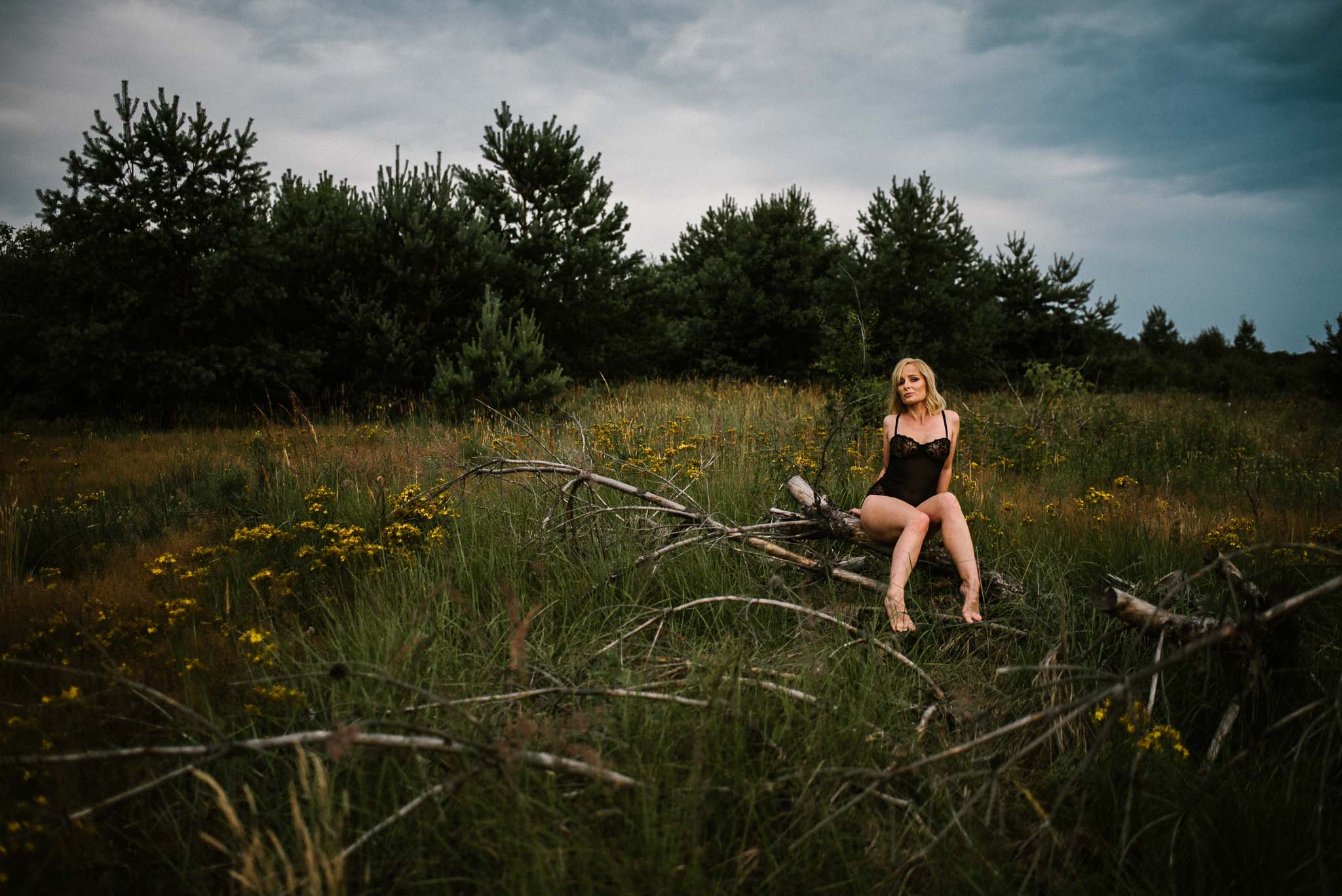 Kobieta siedzi na&nbsp;pniu drzewa na&nbsp;łące w&nbsp;bieliźnie - sesja kobieca sensualna w&nbsp;plenerze Poznań