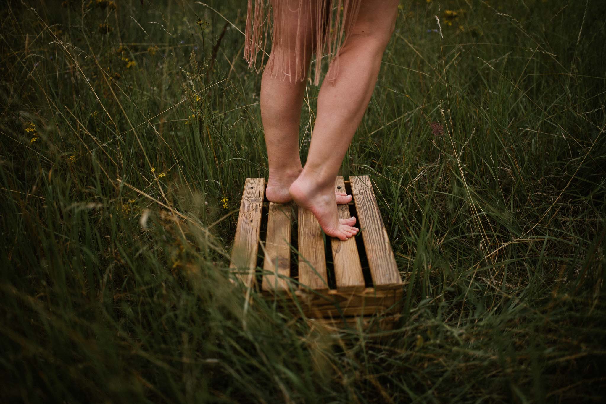 Kobieta stoi na&nbsp;drewnianej skrzynce na&nbsp;łące - sesja kobieca sensualna w&nbsp;plenerze Poznań