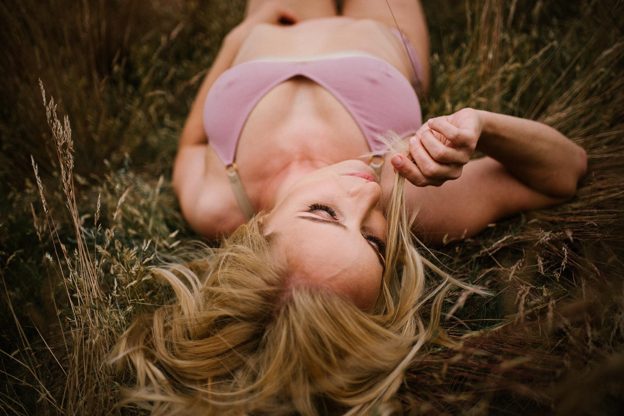 Kobieta leży w&nbsp;bieliźnie na&nbsp;łące i&nbsp;bawi się włosami - sesja kobieca sensualna w&nbsp;plenerze Poznań