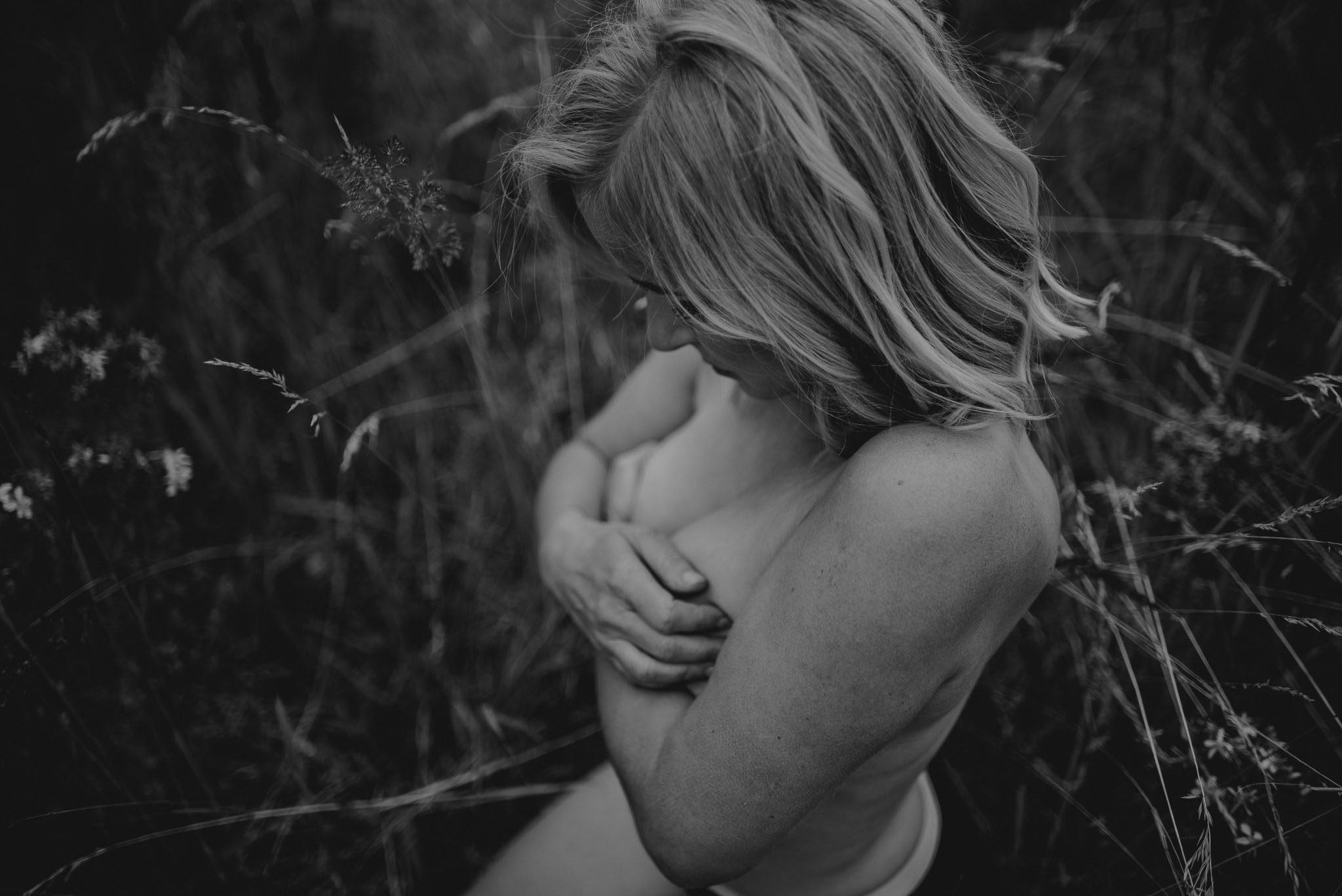 Kobieta zasłania piersi siedząc na&nbsp;łące - sesja kobieca sensualna w&nbsp;plenerze Poznań