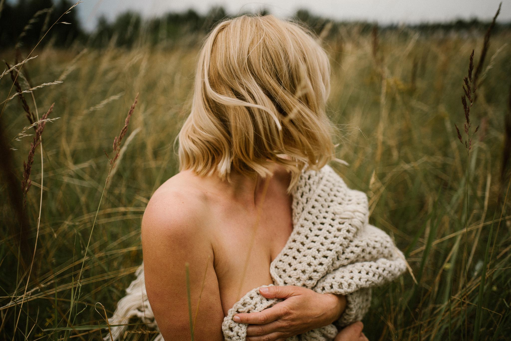 Kobieta zasłania piersi siedząc na&nbsp;łące - sesja kobieca sensualna w&nbsp;plenerze Poznań