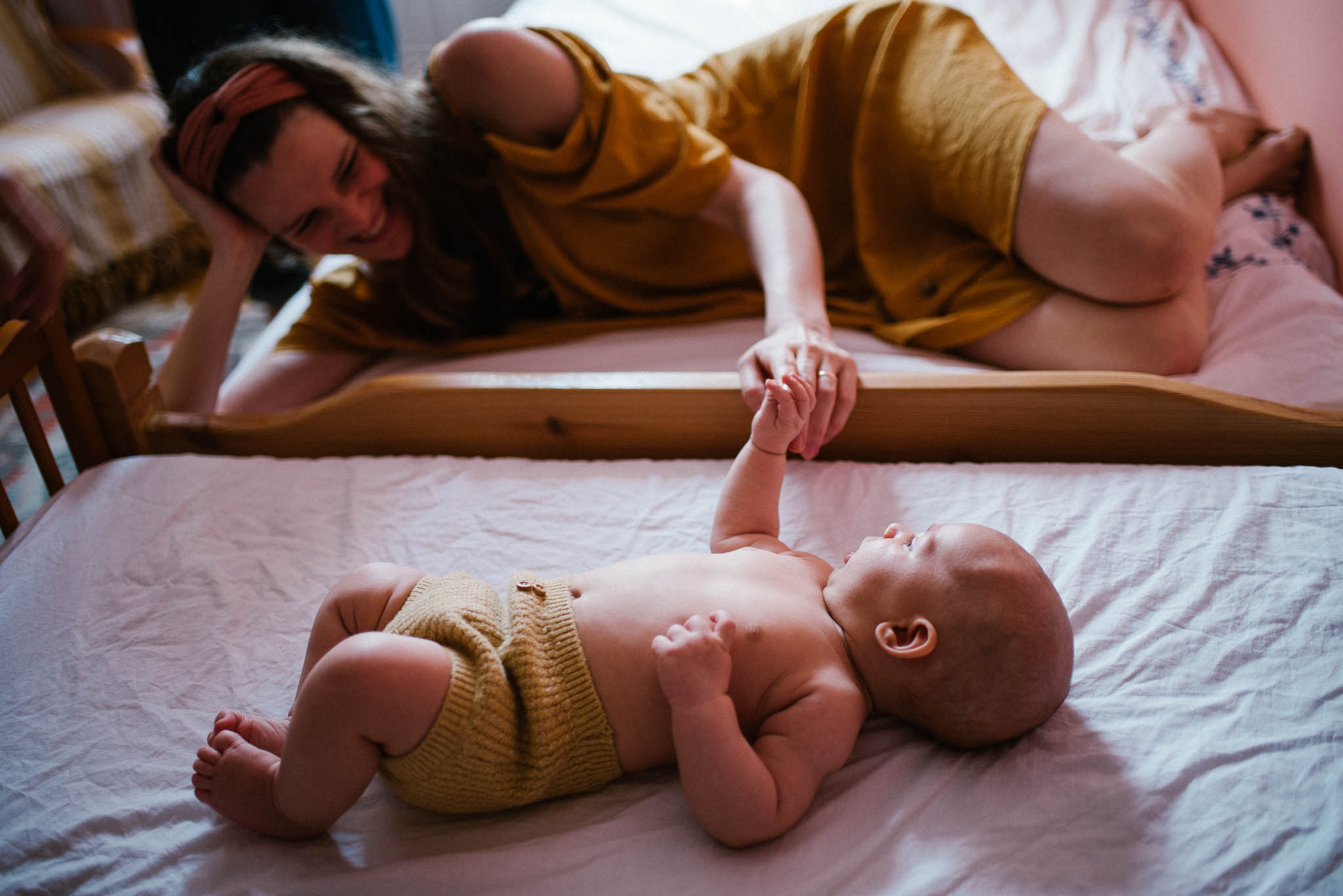 Mama trzyma niemowlę za&nbsp;rączkę, kiedy leży w&nbsp;łóżeczku - sesja niemowlęca lifestyle w&nbsp;domu Poznań