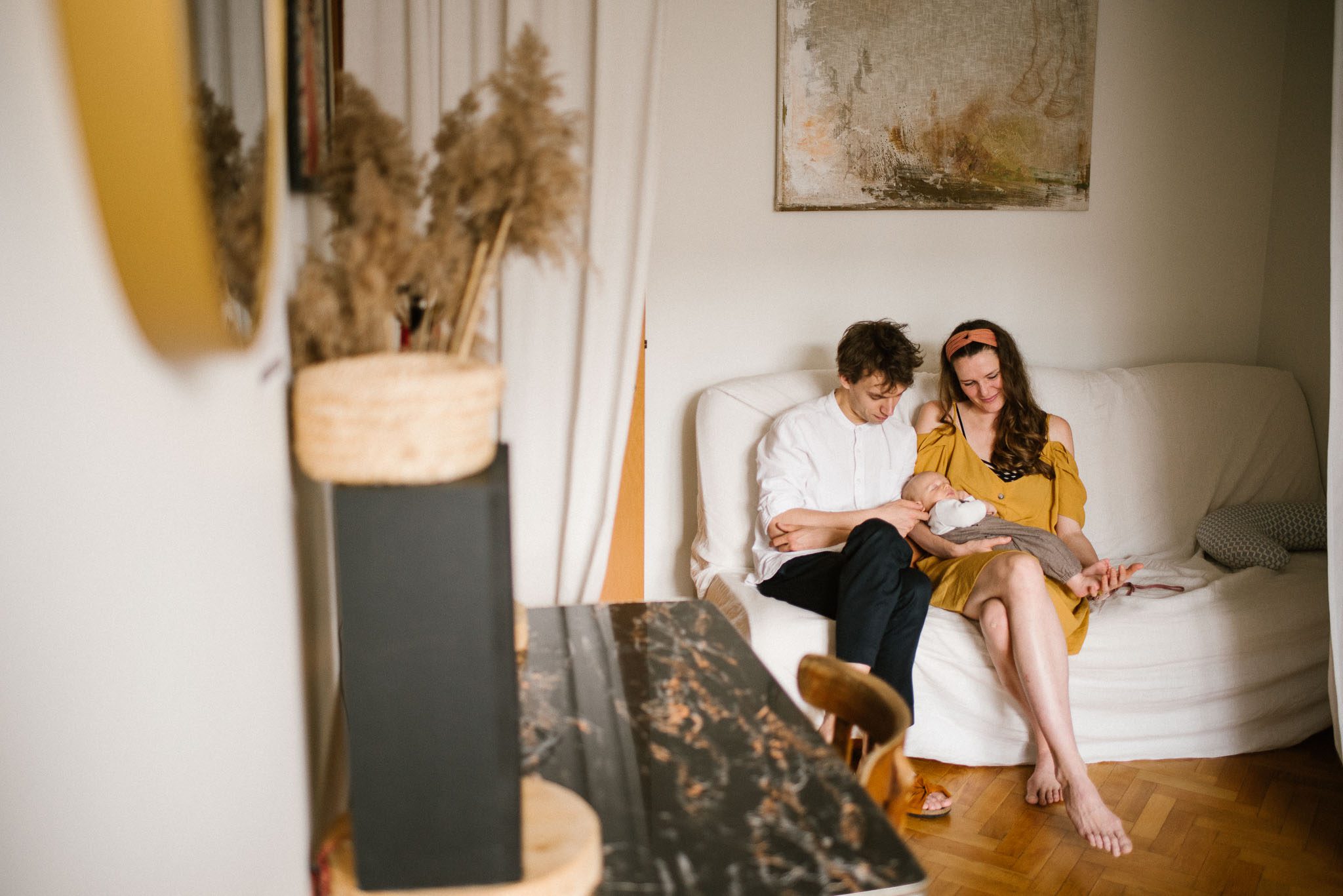 Rodzice z&nbsp;niemowlęciem siedzą na&nbsp;sofie - Sesja niemowlęca lifestyle w&nbsp;domu Poznań